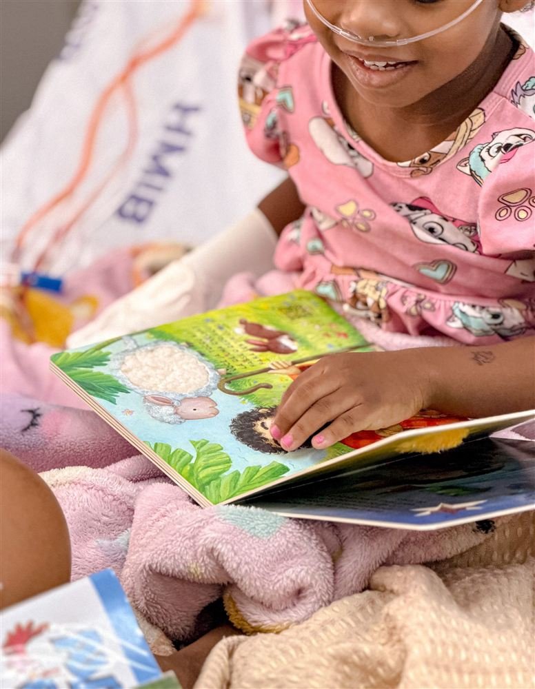 Menina no leito do HMIB folheia um livro infantil do Ler é um Remédio.
